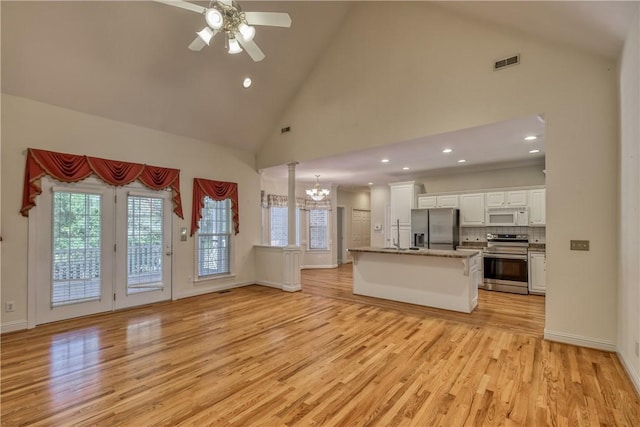 unfurnished living room featuring a chandelier, light wood-type flooring, ceiling fan, high vaulted ceiling, and recessed lighting