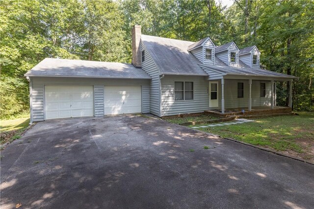 cape cod house with driveway, a garage, a chimney, and covered porch