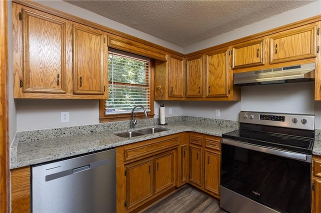kitchen featuring stainless steel appliances, under cabinet range hood, a sink, brown cabinets, and dark wood finished floors
