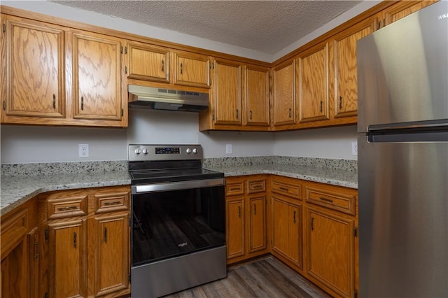 kitchen featuring stainless steel appliances, under cabinet range hood, brown cabinetry, a textured ceiling, and dark wood-style flooring