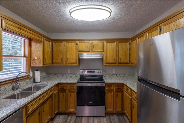 kitchen with stainless steel appliances, a sink, exhaust hood, brown cabinetry, and a textured ceiling