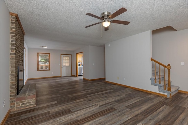 unfurnished living room with ceiling fan, a textured ceiling, wood finished floors, baseboards, and a brick fireplace
