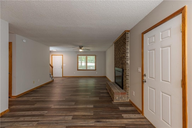 unfurnished living room with dark wood-type flooring, ceiling fan, a fireplace, a textured ceiling, and baseboards