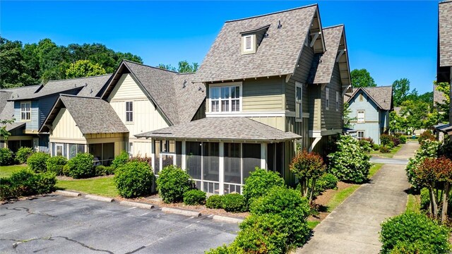view of front of house featuring a sunroom, a shingled roof, uncovered parking, and board and batten siding