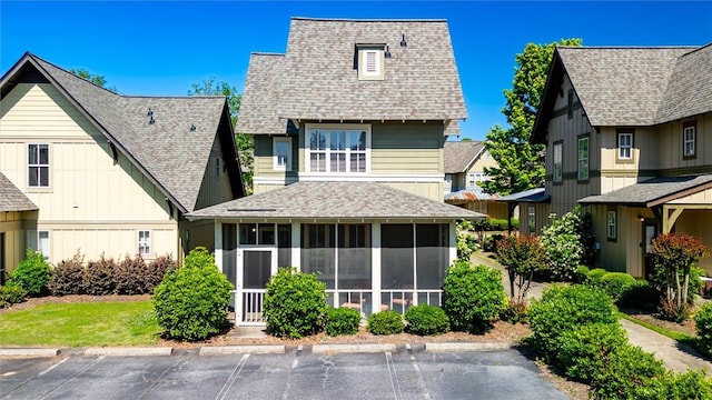 view of front of property featuring uncovered parking, a shingled roof, and a sunroom