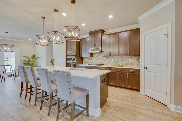 709 Whitemarsh Ave, Simpsonville, SC 29680 - kitchen featuring decorative backsplash, a breakfast bar area, under cabinet range hood, a center island with sink, and light wood finished floors