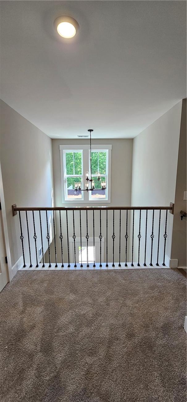 hallway with carpet floors, a chandelier, and baseboards