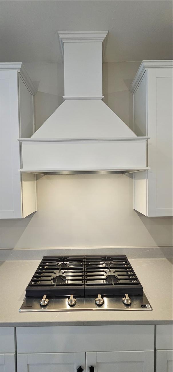 kitchen view of premium range hood, stainless steel gas cooktop, light countertops, and white cabinets
