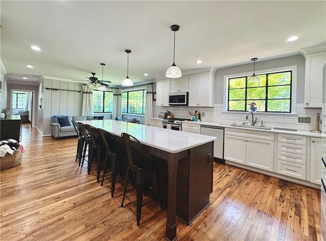 kitchen featuring stainless steel appliances, a sink, light wood-type flooring, open floor plan, and decorative backsplash