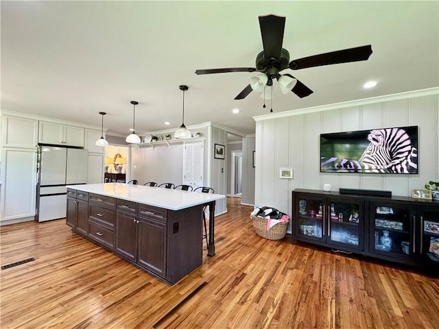 kitchen featuring freestanding refrigerator, dark brown cabinetry, ornamental molding, a ceiling fan, and light wood-type flooring