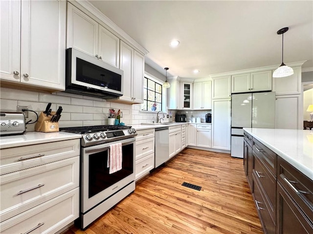 kitchen with stainless steel appliances, light countertops, light wood-style floors, white cabinetry, and backsplash