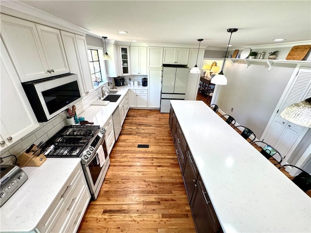 kitchen with appliances with stainless steel finishes, a sink, light wood finished floors, white cabinets, and hanging light fixtures