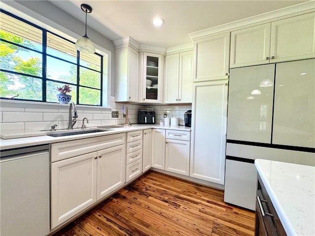 kitchen with a sink, white refrigerator, dishwasher, light countertops, and wood finished floors