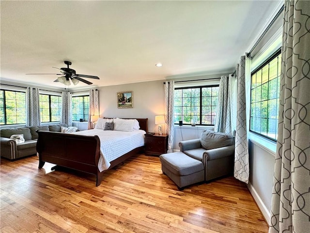 bedroom featuring multiple windows, light wood-style floors, ceiling fan, and ornamental molding