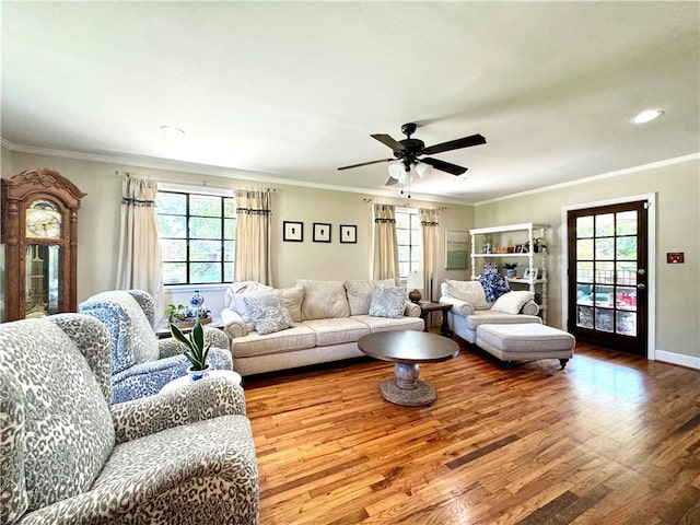 living area featuring wood finished floors, healthy amount of natural light, a ceiling fan, ornamental molding, and baseboards