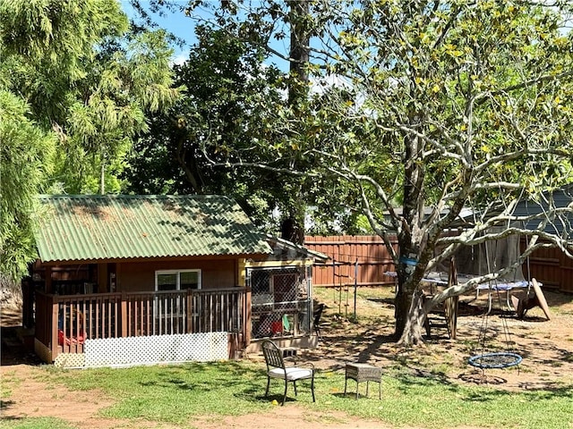 back of property with a trampoline, fence, metal roof, and an outbuilding