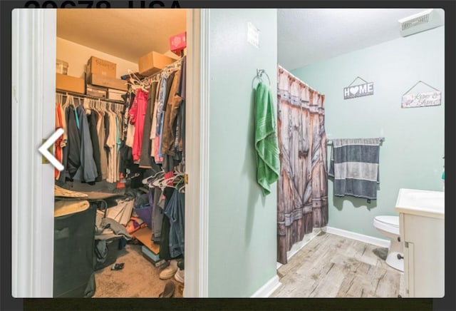 bathroom with vanity, toilet, a walk in closet, and wood finished floors