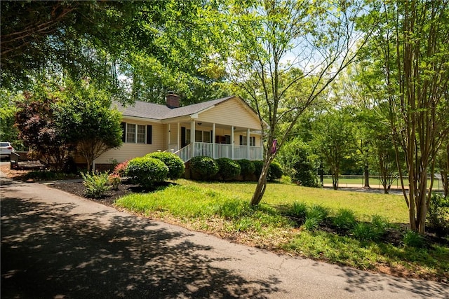 ranch-style home featuring covered porch, a front lawn, and a chimney