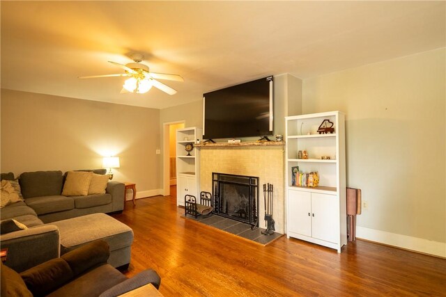 living area featuring a tiled fireplace, dark wood-style floors, baseboards, and a ceiling fan