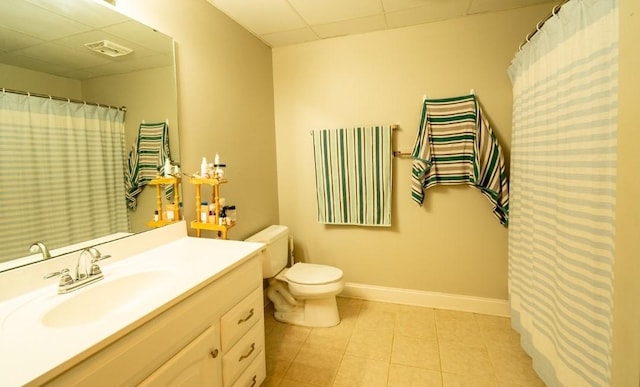 bathroom with a drop ceiling, tile patterned floors, baseboards, vanity, and toilet