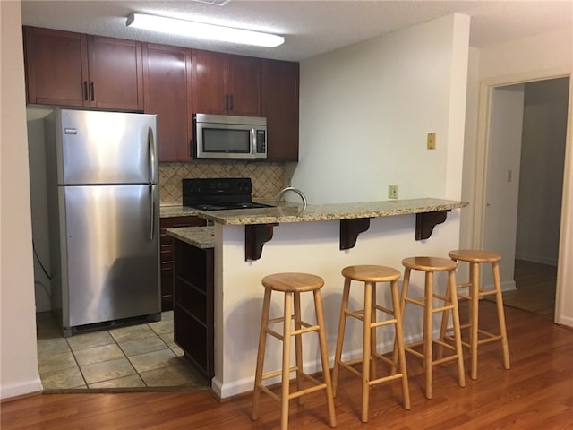 kitchen featuring stainless steel appliances, light wood-style floors, a kitchen bar, light stone countertops, and decorative backsplash