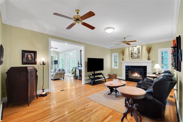 living area with light wood-type flooring, a glass covered fireplace, ceiling fan, ornamental molding, and baseboards