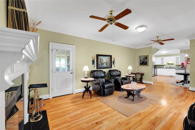 living area with a ceiling fan, light wood finished floors, ornamental molding, and baseboards
