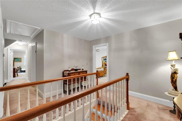 corridor featuring attic access, an upstairs landing, light carpet, a textured ceiling, and baseboards