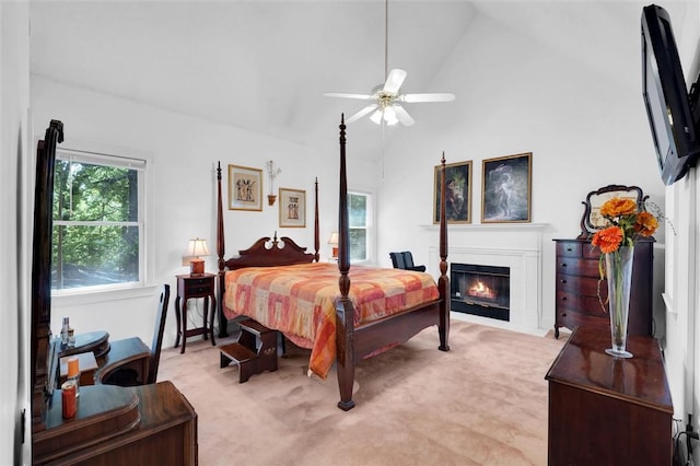 bedroom with lofted ceiling, multiple windows, light colored carpet, a fireplace with flush hearth, and a ceiling fan