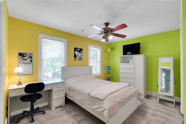 bedroom with light carpet, baseboards, a textured ceiling, a desk, and ceiling fan