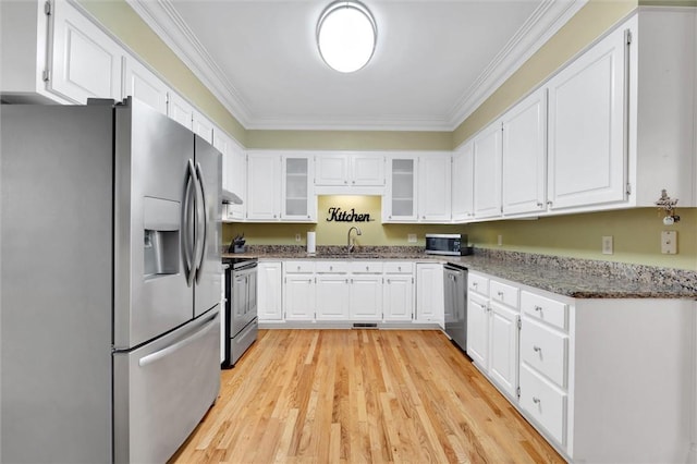 kitchen featuring stainless steel appliances, white cabinetry, crown molding, dark stone countertops, and light wood finished floors