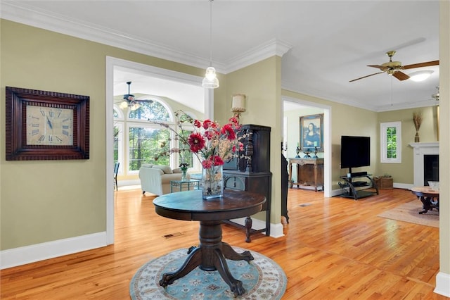 dining room with a ceiling fan, light wood finished floors, baseboards, ornamental molding, and a fireplace