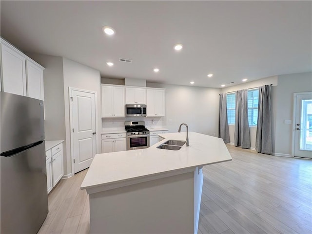 kitchen featuring stainless steel appliances, a sink, light wood-style floors, light countertops, and a kitchen island with sink