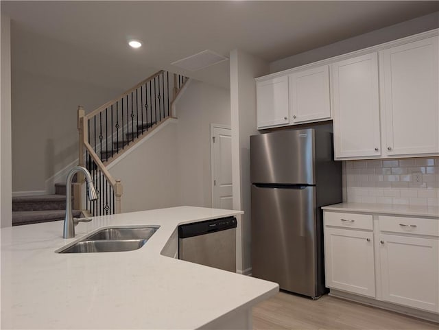 kitchen with appliances with stainless steel finishes, a sink, light wood finished floors, white cabinetry, and backsplash