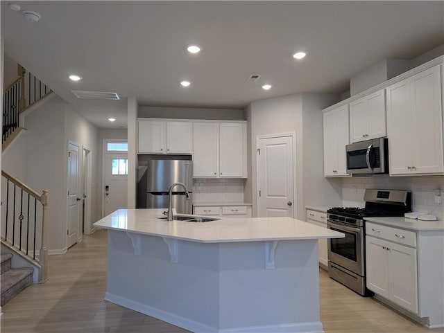 kitchen with appliances with stainless steel finishes, a sink, light wood-type flooring, decorative backsplash, and recessed lighting