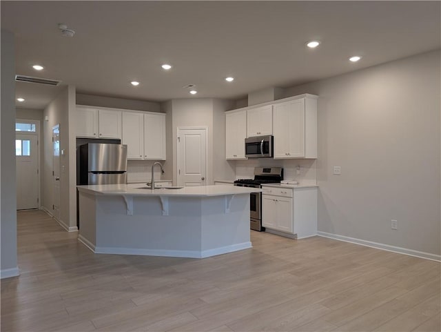 kitchen featuring appliances with stainless steel finishes, a sink, a center island with sink, decorative backsplash, and light wood-type flooring