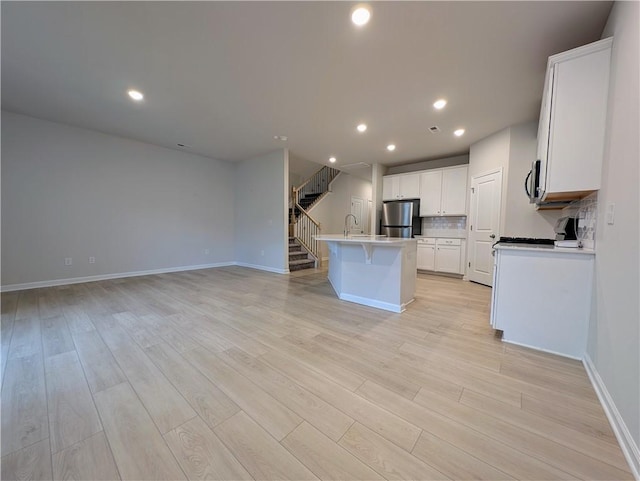 kitchen featuring appliances with stainless steel finishes, open floor plan, light wood-style flooring, baseboards, and a center island with sink
