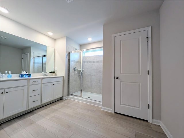 full bathroom with a shower stall, wood finished floors, double vanity, and baseboards