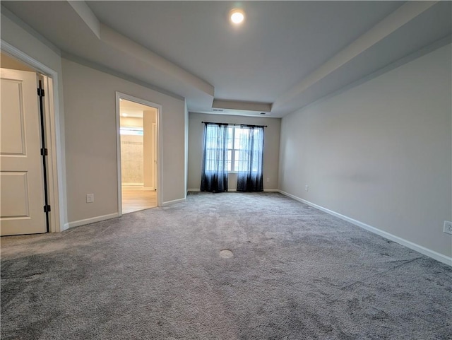 spare room featuring a raised ceiling, carpet floors, and baseboards