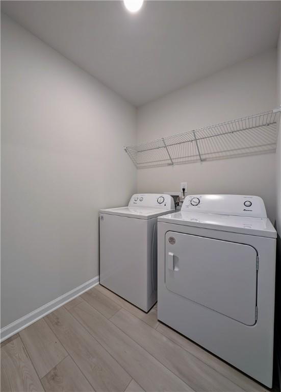 washroom featuring washing machine and clothes dryer, light wood finished floors, and baseboards