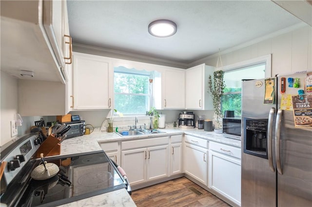 kitchen with stainless steel appliances, a sink, ornamental molding, white cabinetry, and wood finished floors
