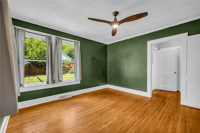 empty room featuring wood finished floors, a ceiling fan, baseboards, and ornamental molding