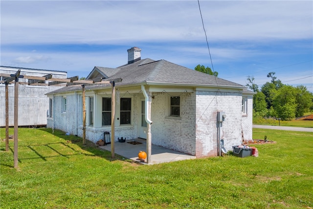 back of house with a yard, a patio area, a chimney, brick siding, and roof with shingles