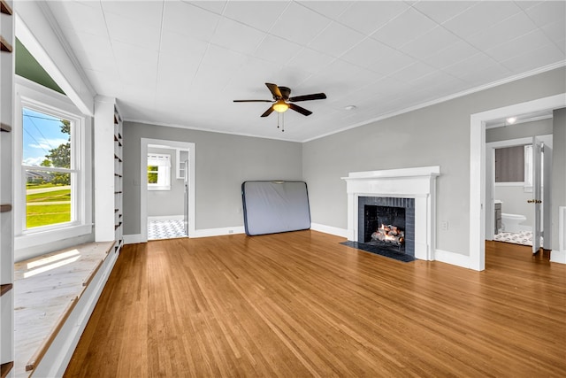 unfurnished living room with wood finished floors, a fireplace, a ceiling fan, baseboards, and ornamental molding
