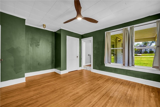 spare room with wood finished floors, baseboards, ceiling fan, and ornamental molding