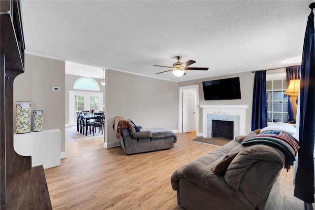 living room featuring a textured ceiling, ceiling fan, light wood-style flooring, a fireplace, and crown molding
