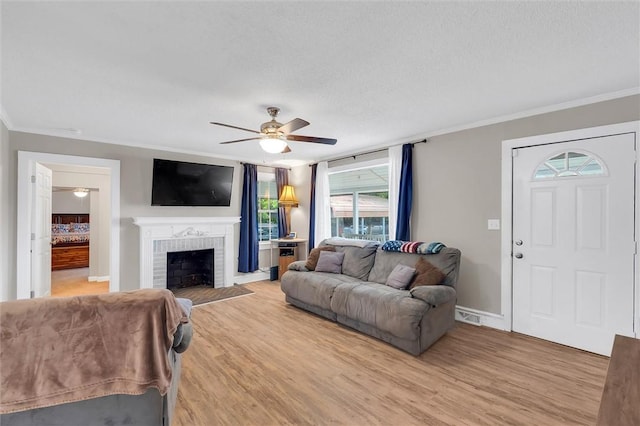 living room featuring a ceiling fan, light wood-type flooring, ornamental molding, a fireplace, and baseboards
