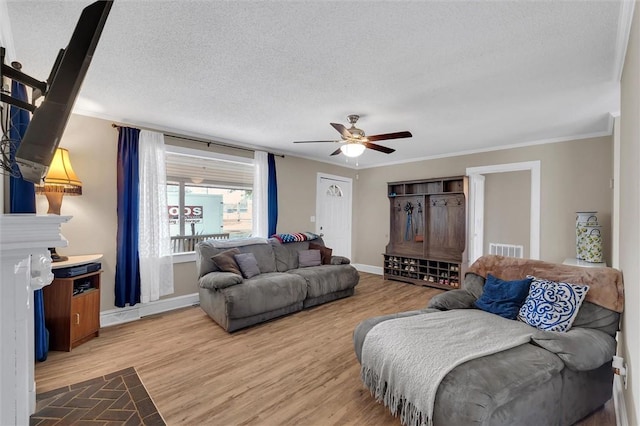 living area featuring ceiling fan, light wood-type flooring, crown molding, baseboards, and a textured ceiling