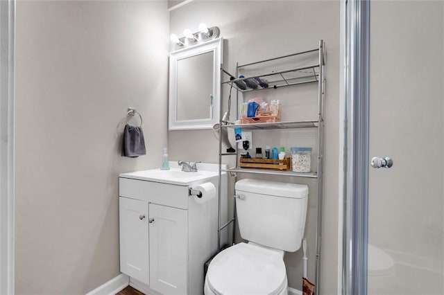 bathroom with toilet, vanity, a shower, and baseboards