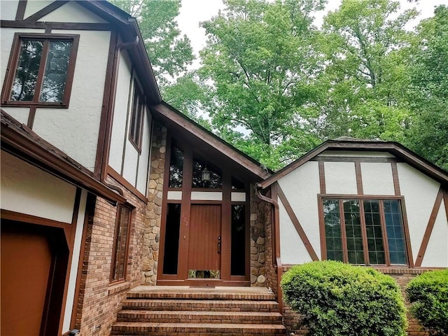 doorway to property featuring stucco siding, stone siding, and brick siding